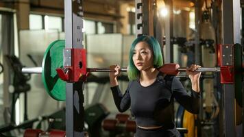 Female bodybuilder doing exercise with heavy weight bar. Fitness woman sweating from squats workout at gym. photo