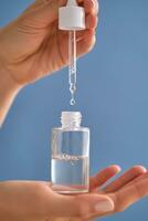 Serum with a pipette in female hands on a blue background. photo