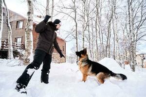 A man plays fetch with a dog in the snowy yard of a house. photo