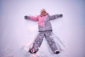 un niña hace un nieve ángel en blanco nieve en invierno. foto