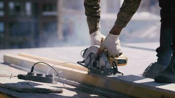 trabajador a un construcción sitio sierras un de madera haz con un eléctrico Sierra video