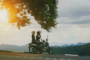couples wearing safety helmet sitting on small enduro motorcycle against beautiful natural mountain scene at khaoyai national park thailand photo