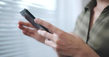 Close up shot of young adult standing in office and typing message via smartphone. video