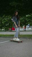 joven niña en un largo camisa montando un largo tablero en un estacionamiento lote, vertical video. video