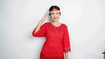 Beautiful Asian woman wearing red kebaya and flag headband giving salute celebrate Indonesian independence day on August 17 isolated over white background video