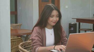 Smiling young Asian woman working remotely from cafe using her laptop, employee getting ready for online video-call interview video