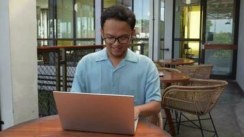 sonriente joven asiático hombre trabajando remotamente desde café utilizando su computadora portátil, empleado consiguiendo Listo para en línea videollamada entrevista video