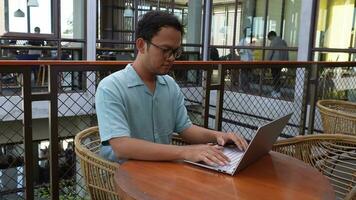 Smiling young Asian man working remotely from cafe using his laptop, employee getting ready for online video-call interview video