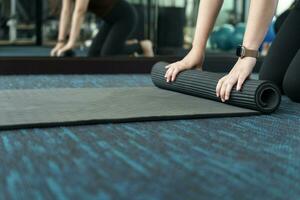 Fitness woman folding exercise mat before working out in yoga studio. rolling Yoga mat  after training healthy lifestyle photo