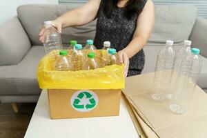 Home recycle eco green zero concept Woman throwing empty plastic bottle in recycling bin with yellow garbage bags at home. photo