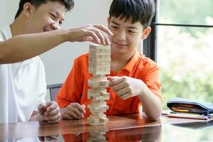 Asian father and son playing wood blocks game Carefree kid playing wood blocks game building constructor from blocks with father at home photo