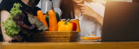 contento dos joven mujer mirando ordenador portátil computadora durante Cocinando juntos en cocina habitación a hogar. dos joven diverso lesbiana mujer gasto hora juntos. lgbt y género identidad concepto foto