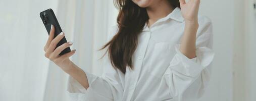 Happy young female in casual clothes smiling and looking at camera while using laptop on bed in bedroom at home photo