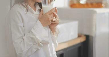 Portrait of a satisfied young asian woman drinking milk from the glass isolated over white background photo