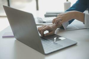 Asian Businesswoman Using laptop computer and working at office with calculator document on desk, doing planning analyzing the financial report, business plan investment, finance analysis concept. photo