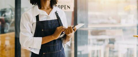 Startup successful small business owner sme beauty girl stand with tablet smartphone in coffee shop restaurant. Portrait of asian tan woman barista cafe owner. SME entrepreneur seller business concept photo