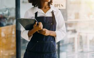 Startup successful small business owner sme beauty girl stand with tablet smartphone in coffee shop restaurant. Portrait of asian tan woman barista cafe owner. SME entrepreneur seller business concept photo