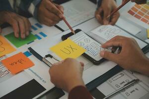 Close up ux developer and ui designer brainstorming about mobile app interface wireframe design on table with customer breif and color code at modern office.Creative digital development agency photo