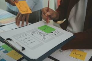 Close up ux developer and ui designer brainstorming about mobile app interface wireframe design on table with customer breif and color code at modern office.Creative digital development agency photo