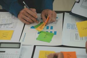 Close up ux developer and ui designer brainstorming about mobile app interface wireframe design on table with customer breif and color code at modern office.Creative digital development agency photo