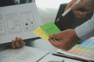 Close up ux developer and ui designer brainstorming about mobile app interface wireframe design on table with customer breif and color code at modern office.Creative digital development agency photo