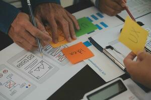 Close up ux developer and ui designer brainstorming about mobile app interface wireframe design on table with customer breif and color code at modern office.Creative digital development agency photo