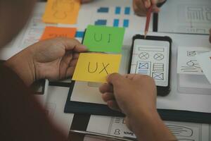 Close up ux developer and ui designer brainstorming about mobile app interface wireframe design on table with customer breif and color code at modern office.Creative digital development agency photo
