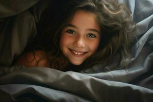 hermosa pequeño niña acostado en cama debajo cobija y sonriente a cámara. ai generado Pro foto