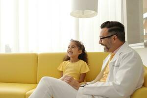 A dentist in a white coat talks about the teeth to a girl in a yellow dress who lies on the couch photo