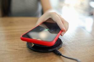 Charging mobile phone battery with wireless device in the table. Smartphone charging on a charging pad. Mobile phone near wireless charger. photo