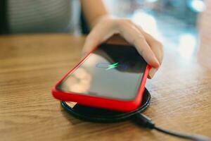 cargando móvil teléfono batería con inalámbrico dispositivo en el mesa. teléfono inteligente cargando en un cargando almohadilla. móvil teléfono cerca inalámbrico cargador. foto