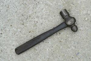 Single dirty old metal or iron hammer with wooden handle laying down on concrete floor. Flat lay photo