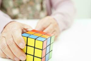 Bangkok, Thailand - May 15, 2022 Asian elderly woman playing Rubik cube game to practice brain training for help dementia prevention and Alzheimer disease. photo