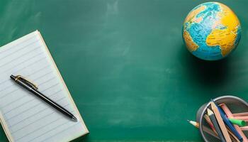 globe, pencil, pen and book on a green blackboard background and empty space on left side photo