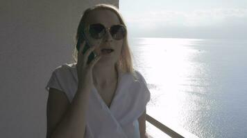 emotioneel vrouw hebben mobiel telefoon praten Aan de balkon met zee visie video