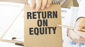 Text RETURN ON EQUITY. on brown paper notepad in businessman hands on the table with diagram. Business concept photo