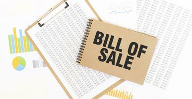 Text BILL OF SALE on brown paper notepad on the table with diagram. Business concept photo