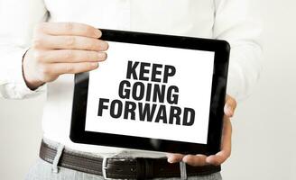 Text KEEP GOING FORWARD on tablet display in businessman hands on the white background. Business concept photo