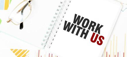 Text WORK WITH US on white notepad, glasses, graphs and diagrams. photo