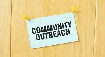 COMMUNITY OUTREACH sign written on sticky note pinned on wooden wall photo