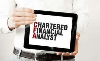 Text CHARTERED FINANCIAL ANALYST on tablet display in businessman hands on the white background. Business concept photo