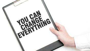 A businessman holds a folder with paper sheet with the text YOU CAN CHANGE EVERYTHING. Business concept. photo