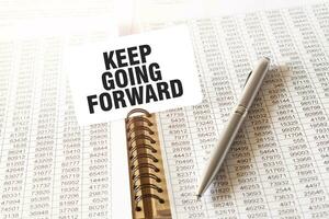 Text KEEP GOING FORWARD on paper card, pen, financial documentation on table photo