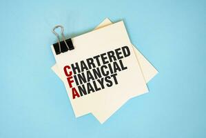 Text CHARTERED FINANCIAL ANALYST on sticky notes with copy space and paper clip isolated on red background.Finance and economics concept. photo