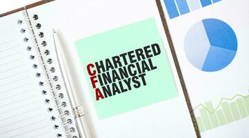 Green card on the white notepad. Text CHARTERED FINANCIAL ANALYST. Business concept photo