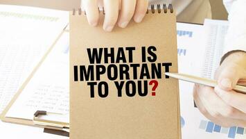 Text WHAT IS IMPORTANT TO YOU on brown paper notepad in businessman hands on the table with diagram. Business concept photo