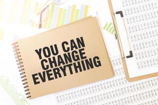 Business up graph on a sheet of craft colour Notepad with YOU CAN CHANGE EVERYTHING sign. Notepad on desk with financial documentation photo