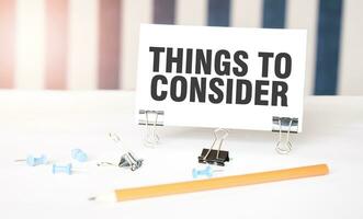 THINGS TO CONSIDER sign on paper on white desk with office tools. Blue and white background photo