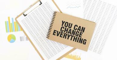 Text YOU CAN CHANGE EVERYTHING on brown paper notepad on the table with diagram. Business concept photo