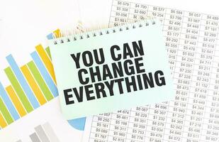 Green notepad on financial documentation. Text YOU CAN CHANGE EVERYTHING. Business concept photo